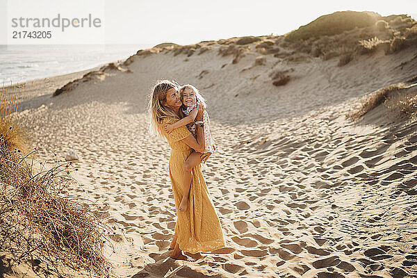 Mother and daughter hugging at beach on summer day