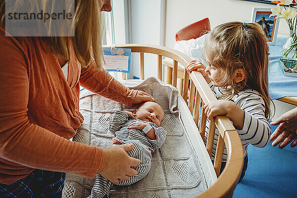 Newborn baby sleeping in hospital bassinet crib with family around