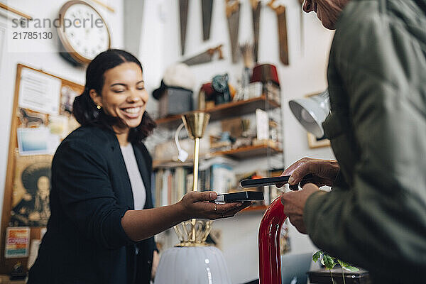 Female shop owner receiving payment from customer via tap to pay method at antique store