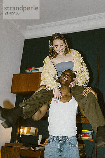 Happy young man carrying girlfriend on shoulder at home