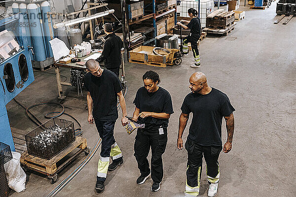 High angle view of male and female warehouse worker in black uniform discussing while walking in factory