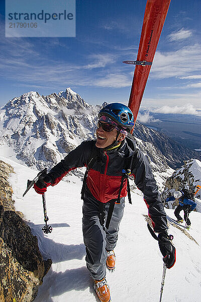 Two male backcountry skiers make it to the top of Mt. Buck on a gorgeous Spring day. Ice ax in hand and smile on his face.