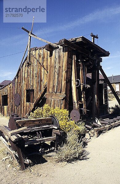 Decayed  crooked wooden shed with technical equipment in front of it in the former gold mining town of Bodie. Colour picture  Technical equipment in front of a decayed  crooked wooden shed in the former gold mining town Bodie. Colour picture  vertical format