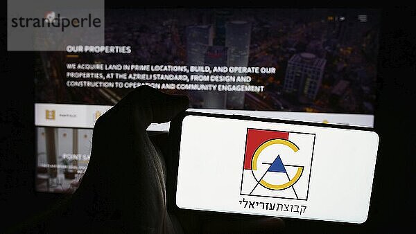 Stuttgart  Germany  07-08-2024: Person holding mobile phone with logo of Israeli real estate company Azrieli Group Ltd. in front of business web page. Focus on phone display  Europe