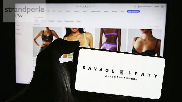 Stuttgart  Germany  05-15-2024: Person holding mobile phone with logo of American fashion company Savage X Fenty in front of business web page. Focus on phone display  Europe