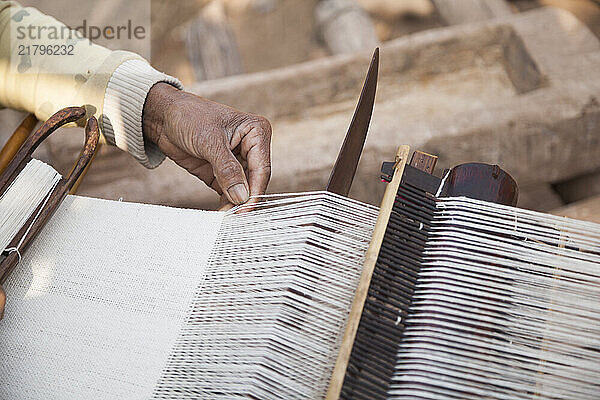 Woman weaving long sheet of fabric on small hand-operated loom in Ban Phu Muang  Laos