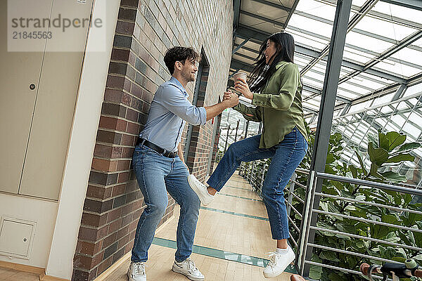 Happy businesswoman holding hand of colleague and jumping in corridor