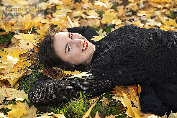 Smiling woman lying on orange leaves in park