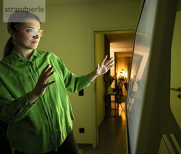 Woman with smart glasses and gesturing near device screen at home