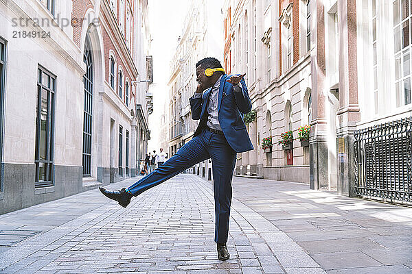 Cheerful mature businessman wearing wireless headphones and dancing on street