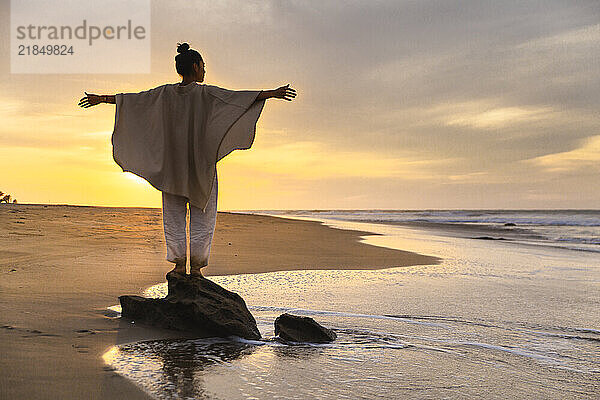 Carefree woman wearing poncho and standing on rock under cloudy sky