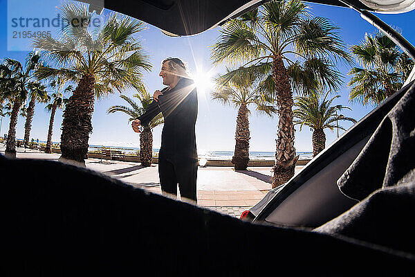 Surfer wearing wetsuit getting ready on the beach with palm trees