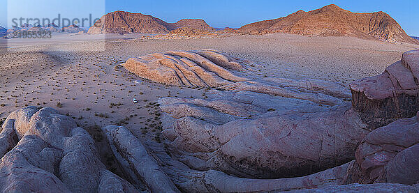 A jeep is parked at the base of pink sandstone formations at dusk in Wadi Rum  Jordan.