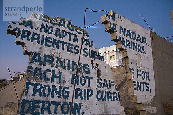 A broken wall frames a house built with heavy reinforcements on El Faro Beach near Ensenada  Baja California  Mexico.