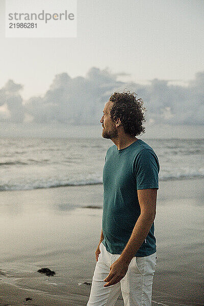 Millenial man walking barefoot on the beach at sunset