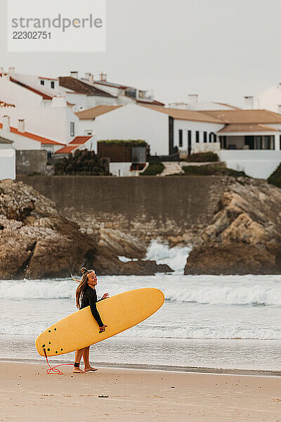 A female surfer with a yellow surfboard walks along the shore i