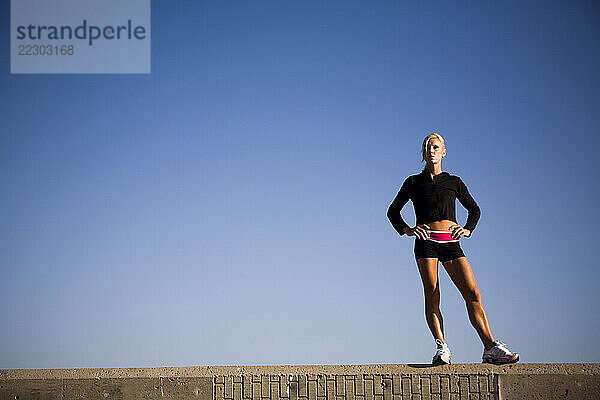 A women poses in ahtletic wear on a cement wall in Oceanside  CA.