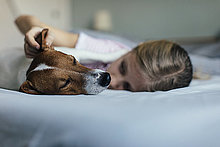 Mädchen liegt auf Bett und kitzelt ihren Hund
