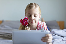 Porträt eines blonden, auf dem Bett liegenden Mädchens mit Lolli mit digitalem Tablett